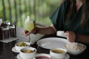a woman is holding a glass of orange juice on a table with food at Jeevan Homestay & Ayurvedic Yoga Retreat in Kovalam