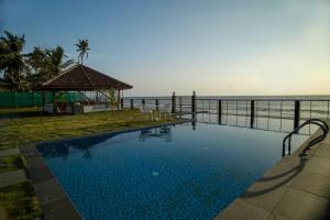 a swimming pool with a gazebo next to the ocean at Ragas - Marari Beach Villa By Perfect Stays in Alleppey
