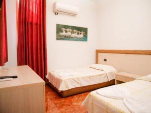 a hotel room with two beds and a desk and red curtains at Hotel Serenity in Tirana
