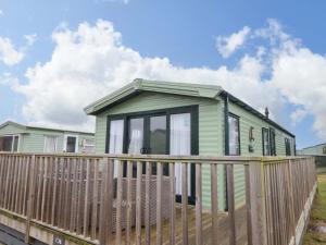 a green tiny house with a wooden fence at Sea Breeze C38 Dyffryn Seaside Estate in Dyffryn