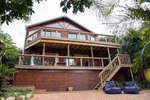 a large wooden house with a balcony and stairs at 10d Mimosa - The Spot - by African Perfection in Jeffreys Bay