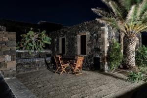 een patio met 2 stoelen, een tafel en een palmboom bij Dammusino A-mare in Pantelleria +10 foto's
