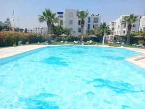a large swimming pool in a resort with palm trees at Lappartement de la Marina: Vue mer et port in Yasmine