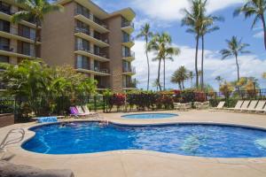 a pool in front of a building with palm trees at Kauhale Makai 122 in Kihei