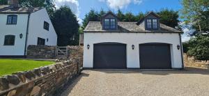 a white house with two garage doors and a stone wall at White Cottage Loft in Newtown Limford