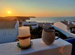 een kaars en een kopje op een tafel met de zonsondergang bij Casa Calma in Salema