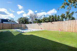 un patio trasero con una valla y una pista de tenis en Solara House with Heated Pool and Cinema Room, en Safety Beach