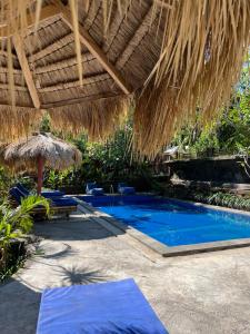 a resort with a swimming pool with a straw umbrella and chairs at Alfa Kuta in Kuta Lombok