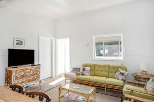 un salon avec un canapé et une télévision dans l'établissement Retro Beach Cottage - classic surf getaway, à Kioloa