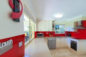 een keuken met rode muren en witte kasten bij Pelican Beach House - 50m from inlet & playground in Narrawallee