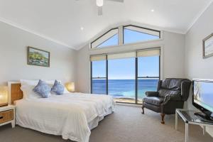 a bedroom with a bed and a chair and a television at South Pacific Beach House - direct beach access in Ulladulla
