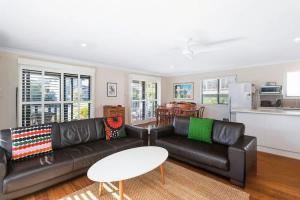 a living room with a black leather couch and a table at Bawley Beach Bungalow in Bawley Point