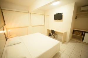 um quarto com uma cama branca, uma secretária e uma televisão em Hotel Itajaí Tur - Itajaí Navegantes em Itajaí