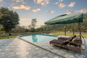 a swimming pool with chairs and an umbrella at SaffronStays Sukh Saklana Haveli Royalty Rooms - Forest-view stay with pool, expansive lawns & dining near Rishikesh and Dehradun Airport in Dehradun