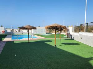 eine Gruppe von Strohschirmen auf einer Wiese mit einem Pool in der Unterkunft Casa Nova WINTER: Casa costera en San Juan de los Terreros - ES-376-38 in Pulpí