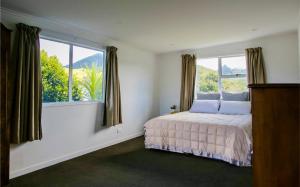 a bedroom with a bed and two windows at Coastal Retreat - Whiritoa Holiday House in Whiritoa