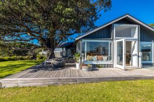 a house with large windows and a wooden deck at Palm Beach Retreat - Be My Guest Waiheke in Waiheke Island