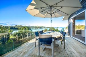 a dining table and chairs on a deck with an umbrella at Shelley Beach Homestead in Waiheke Island