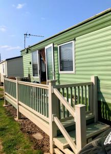 a green mobile home with a wooden deck at PD Wonderwall Caravan, Direct beach access & Beds made on arrival & GCH in Ingoldmells