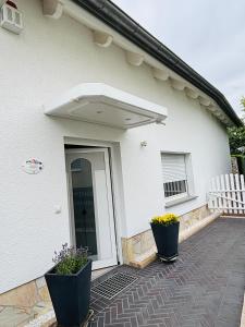 a white house with an open door with two plants at Casa Armonia Halle- Ruhige Ferienwohnung am Pestalozzipark und Gesundbrunnen in Halle an der Saale