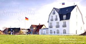 舍恩贝里耶海滩Strandvilla Seelust的田野里插着旗帜的白色大房子