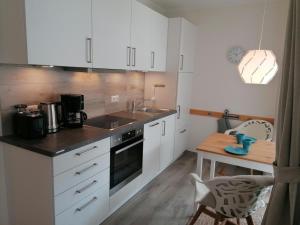 a kitchen with white cabinets and a sink and a table at Ferienwohnung am Kirchturm in Fehmarn