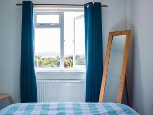 a bedroom with a window with blue curtains and a mirror at Holiday Home Creag Dubh by Interhome in Camastianavaig