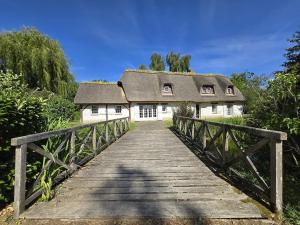 a bridge leading to a house with a roof at Chaumière entre rivière & champs, piscine privée in Verneuil d’Avre et d’Iton