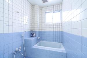 ein weiß gefliestes Bad mit einer Badewanne und einem Fenster in der Unterkunft わったー家あぱらぎ館 in Ishigaki-jima