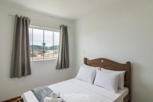 a bed with white pillows and a window in a room at Apto Vista Mar Lateral a 120m da Praia EEI0303 in Itajubá