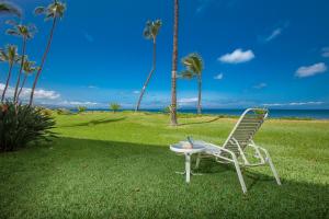 a chair and a table in the grass with palm trees at Sugar Beach 132 - MCH in Kihei