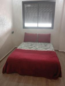 a bed with a red comforter and a window at للا ربيعة بيتي in Kenitra