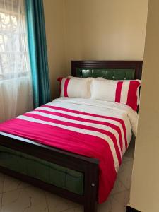 a bed with a red and white blanket and a window at Moods Holiday Homes in Bulenga