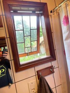 a man taking a picture of a window in a bathroom at caminho das montanhas chalé in Itanhandu