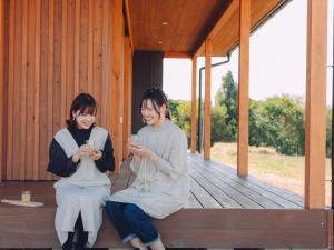 two women sitting on a porch looking at their cell phones at Cider Barn &more in Iida