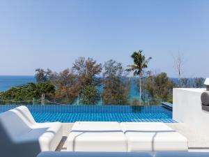 uma piscina com cadeiras brancas e o oceano em Villa Sammasan by Elite Havens em Praia de Surin