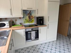 eine Küche mit weißen Schränken und einem Herd mit Backofen in der Unterkunft Maple Cottage in Bourton on the Water