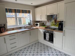 eine Küche mit weißen Schränken und einer Spüle und einer Mikrowelle in der Unterkunft Maple Cottage in Bourton on the Water