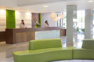 a lobby with a green couch and two people at JS Sol de Alcudia in Port d'Alcudia