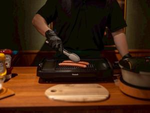 a person is cutting a hot dog on a grill at HOTEL RELIEF Kokura Station in Kitakyushu