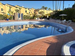 a swimming pool with tables and chairs and some buildings at Meloneras Garden Bungalow in Meloneras