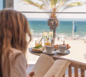 a woman sitting at a table with food and drinks at Meraki Beach Hotel - Only Adults in Playa Pobla de Farnals