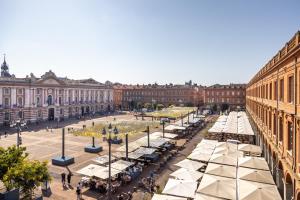 Una plaza de la ciudad con mesas y sombrillas frente a los edificios. en Capitole Horizon, en Toulouse
