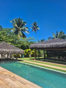 a swimming pool withiki umbrellas and palm trees at Casa Guaimbê com Rooftop e piscina privativa in São Miguel dos Milagres