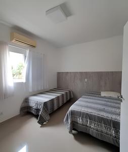 two beds in a white room with a window at Casa na Morada da Praia - Q83 in Bertioga +53 photos