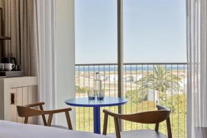 a room with a bed and a table and a balcony at Amarello Hotel Praia Santo André, Tapestry Collection by Hilton in Santiago do Cacém