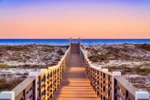 a wooden boardwalk to the beach at sunset at Whitecap - Beachfront Gem with Pool & Elevator in Orange Beach