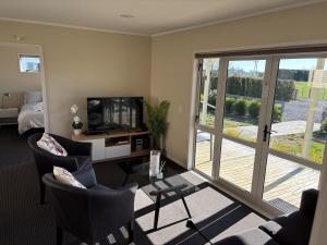 a living room with chairs and a television and a balcony at Havelock Cottage - Pukeko Nest in Havelock North