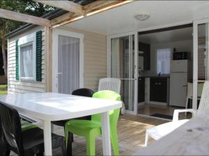 Una mesa blanca y sillas verdes en un patio. en Mobil-home 25m² avec Terrasse à Brétignolles-sur-Mer - API-1-52-341, en Bretignolles-sur-Mer