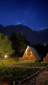 a wooden cabin at night with a fence and mountains at Fortyard Cottages Hunza in Karimabad Hunza